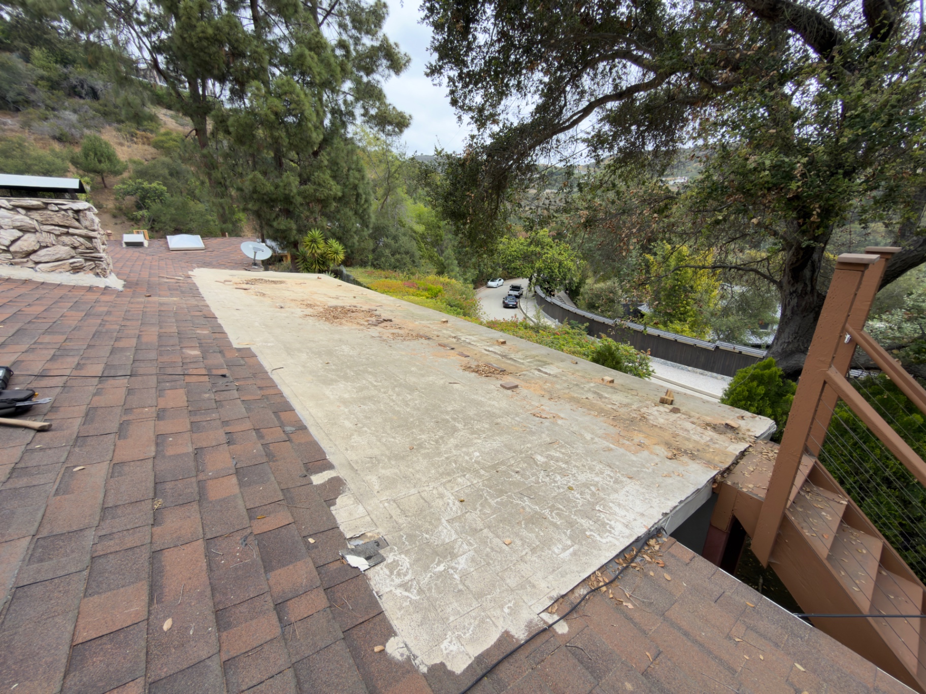 Worn torch-down roof section before repair, surrounded by shingle roofing